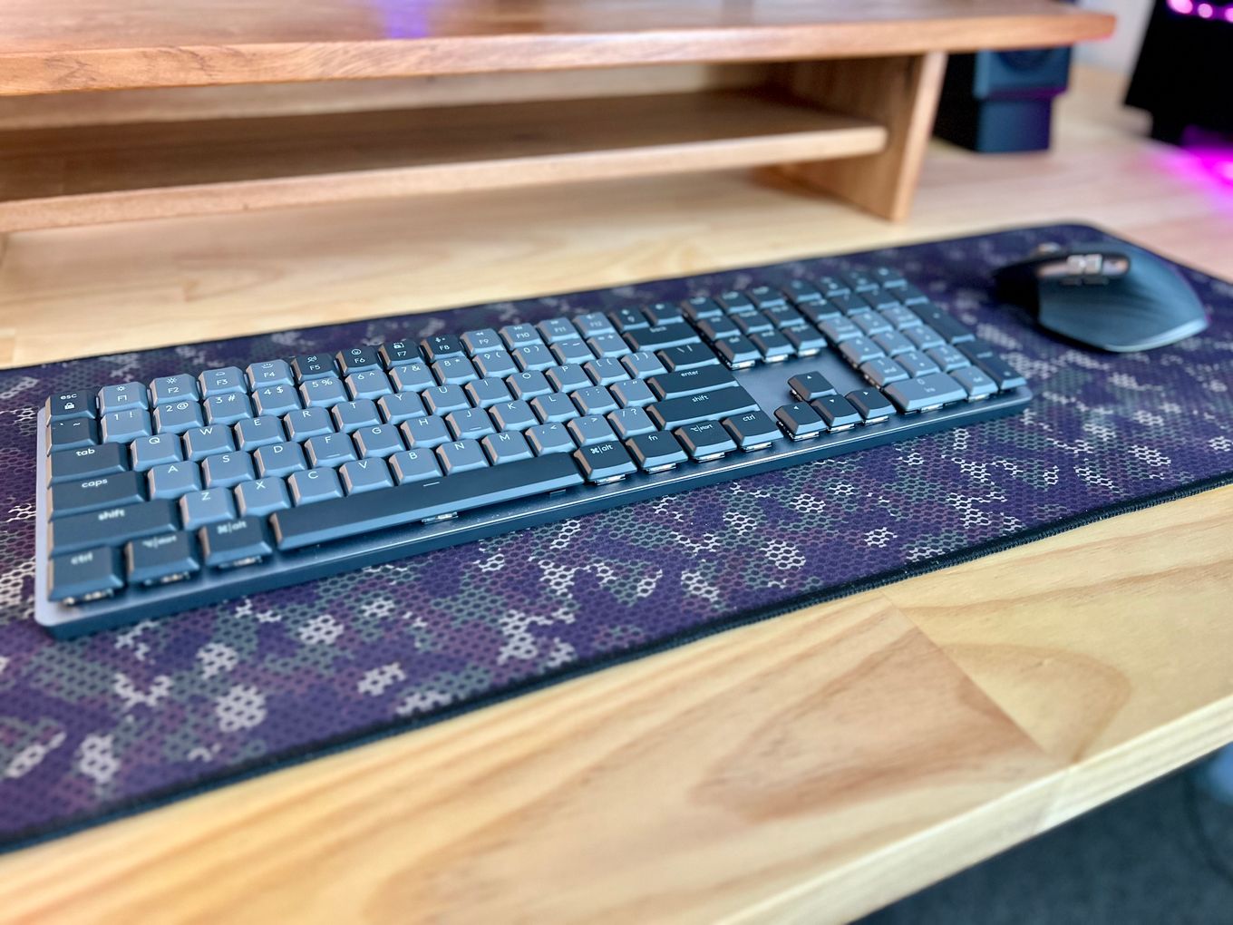 A Logitech MX Mechanical keyboard and MX Master 3S mouse on a camouflage mouse mat on a wooden desk